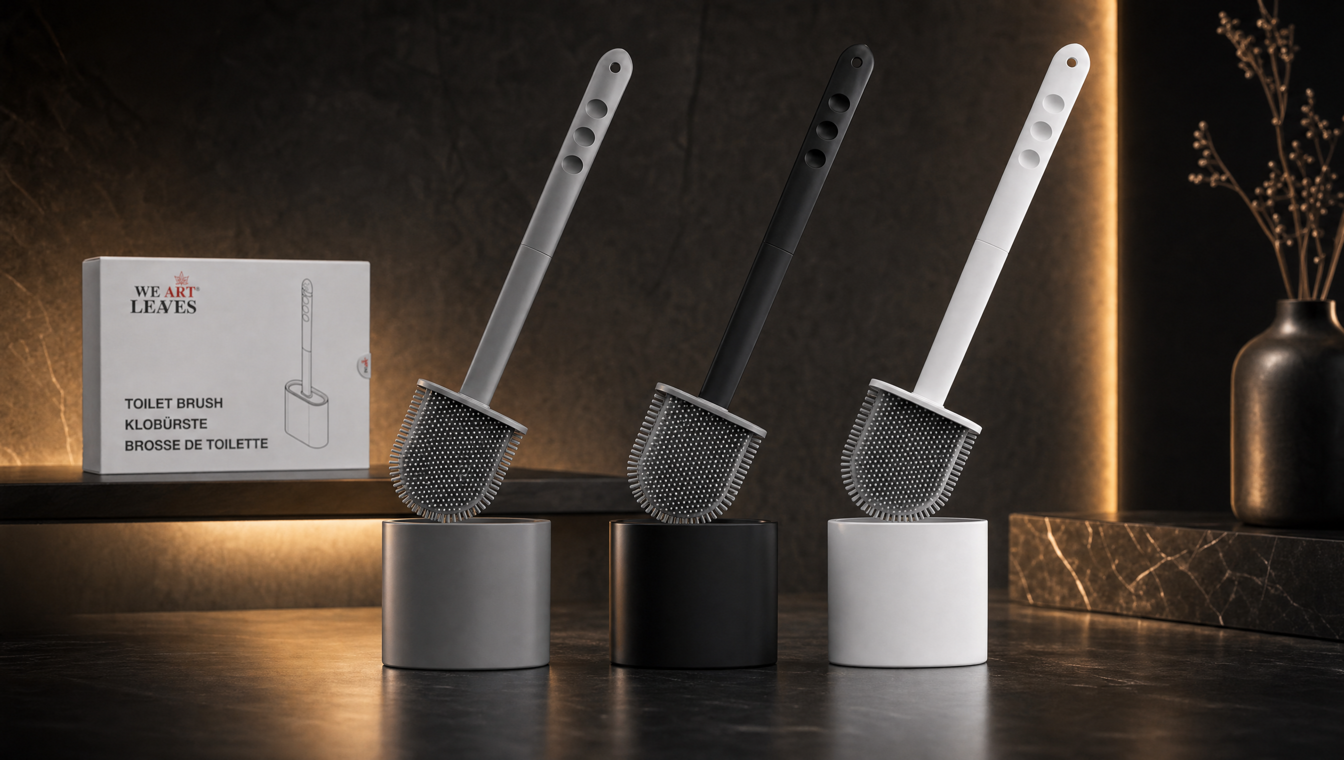WE ART LEAVES premium silicone toilet brushes in grey, black and white on a dark marble surface, warm cinematic lighting